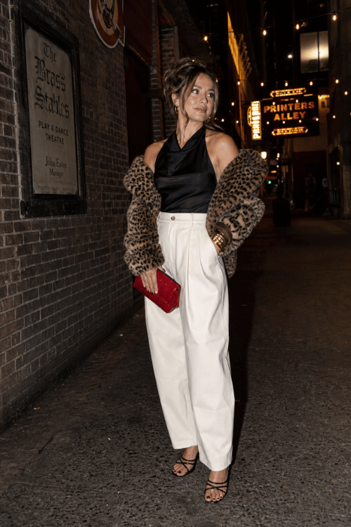 Woman wearing a black satin halter top with white high-waisted trousers and a leopard faux fur jacket.