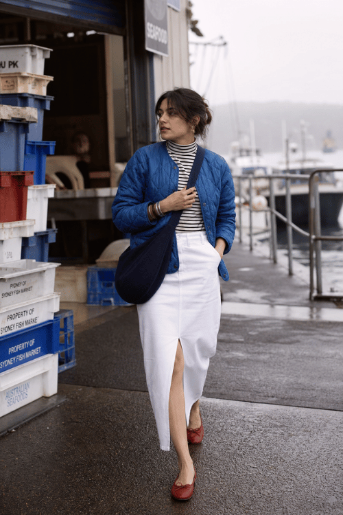 Woman wearing a blue quilted jacket with a striped turtleneck and a white midi skirt.