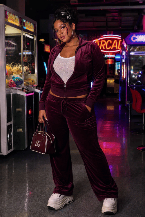 Woman wearing a burgundy velour tracksuit with chunky sneakers and a top-handle bag.