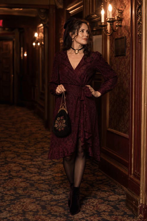 Woman wearing a burgundy wrap dress with velvet ankle boots and an embroidered handbag.