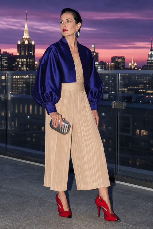 Woman wearing a champagne pleated jumpsuit with a royal blue satin shrug and red heels.
