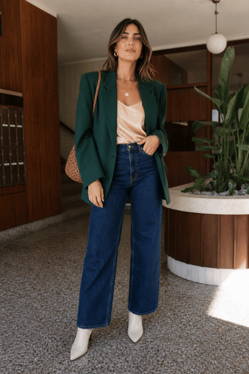 Woman wearing a dark green blazer with dark wash jeans and white pointed toe boots.