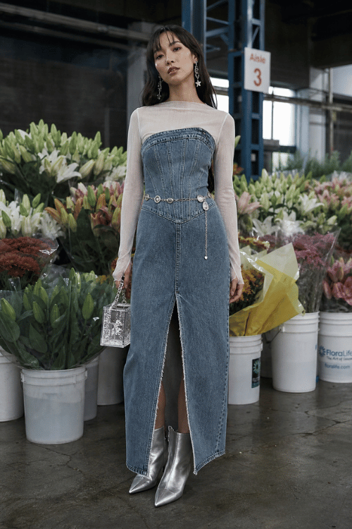 Woman wearing a denim corset maxi dress with a sheer top and silver ankle boots.
