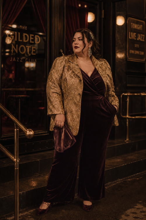 Woman wearing a gold brocade blazer over a burgundy velvet jumpsuit.