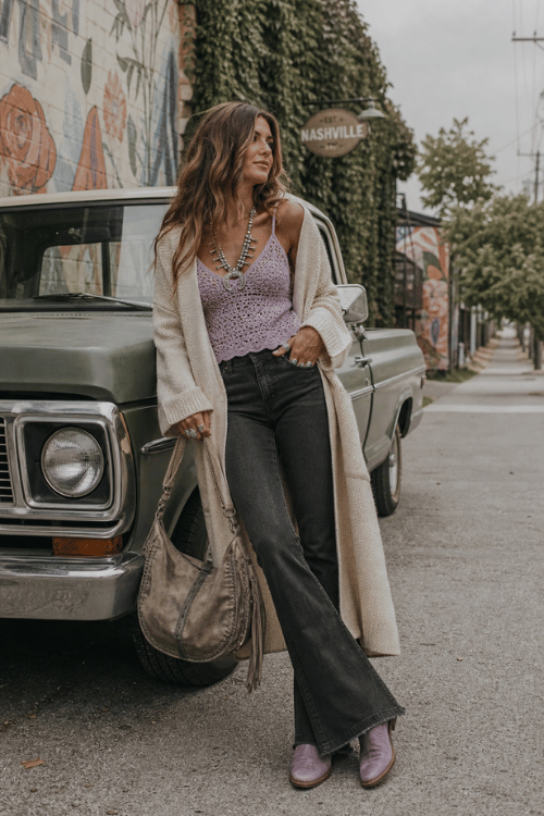 Woman wearing a lavender crochet camisole, long cardigan, black flare jeans, and lavender ankle boots on a Nashville street.
