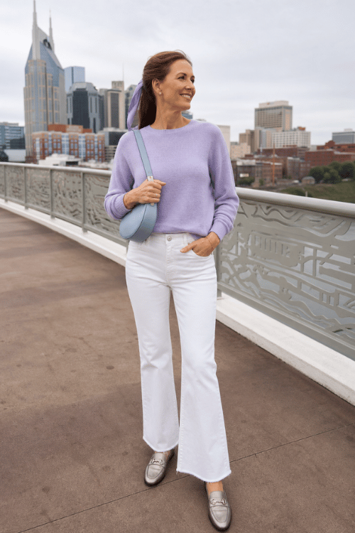 Woman wearing a lavender sweater, white jeans, and silver loafers overlooking the Nashville skyline.