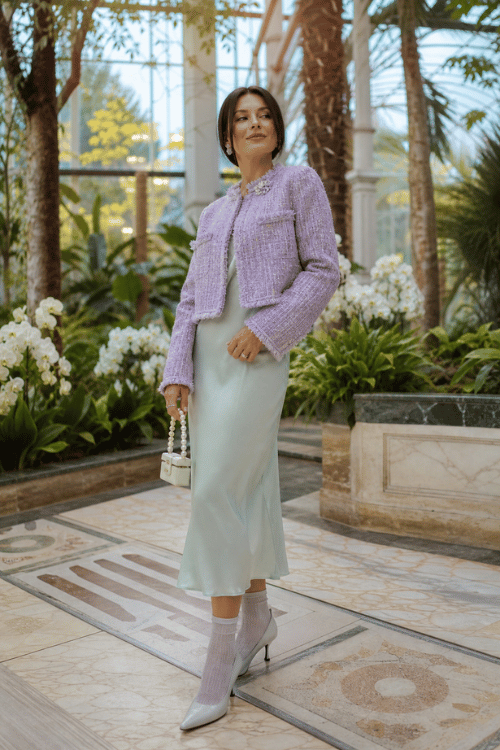 Woman wearing a lilac tweed jacket with a pale blue satin slip dress and silver ankle boots.