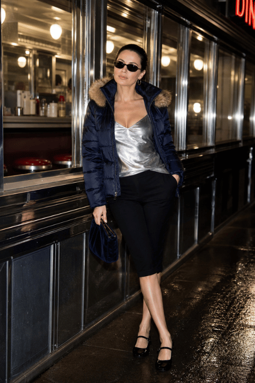 Woman wearing a navy puffer jacket with a silver camisole and black midi skirt.