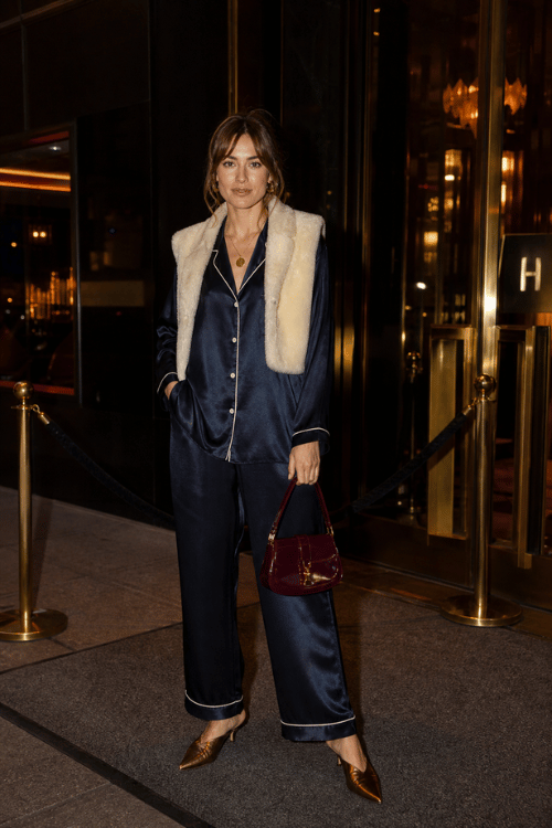 Woman wearing a navy satin pajama set with a faux fur vest and metallic pointed heels.