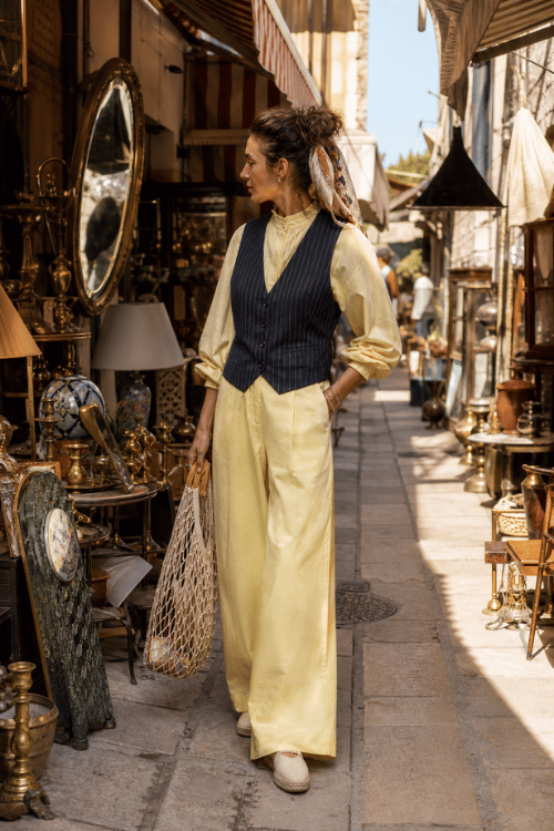 Woman wearing a pale yellow jumpsuit with a navy pinstripe vest and canvas tote bag.