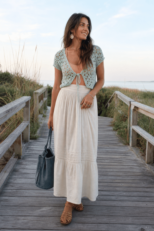 Woman wearing a sage crochet cardigan with a white maxi skirt and tan woven sandals.