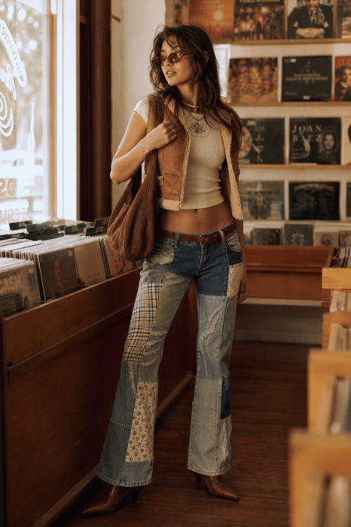 Woman wearing a shearling vest with patchwork jeans and pointed ankle boots.