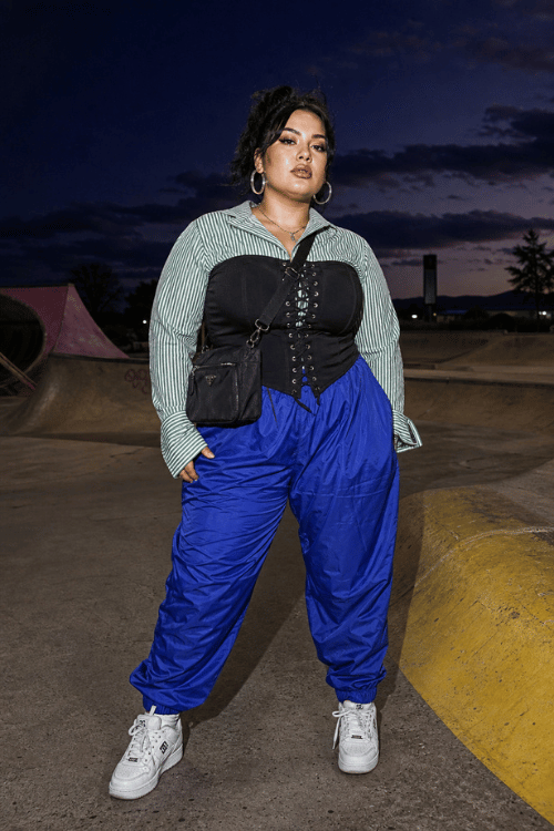Woman wearing a striped shirt with a black corset and blue jogger pants.
