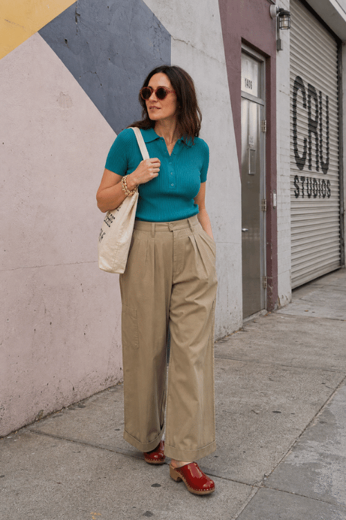 Woman wearing a teal knit polo, khaki wide-leg trousers, and red clogs on a city sidewalk.
