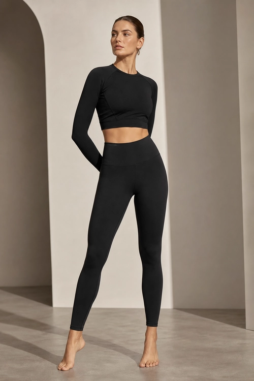 A woman wears a black long-sleeve cropped top and high-waisted leggings with small hoop earrings.