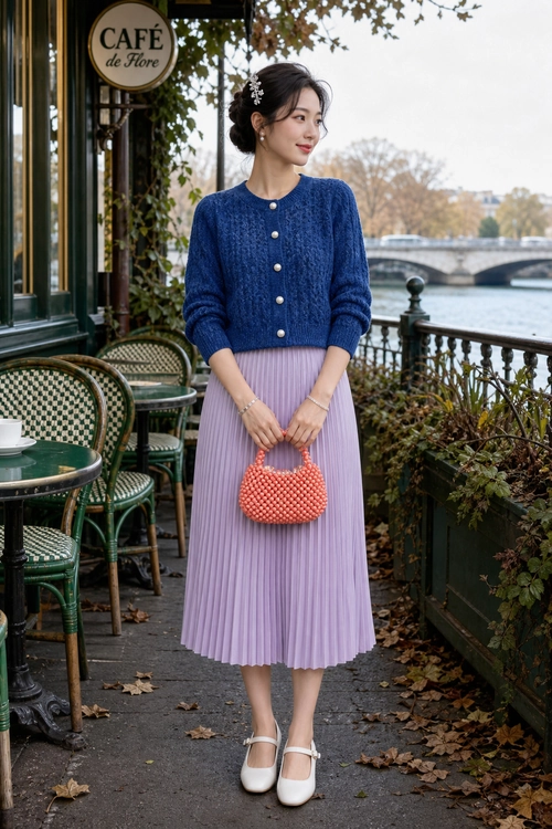 Blue Cardigan and Lavender Pleated Skirt Outfit A woman wears a blue knit cardigan with a lavender pleated midi skirt, white strap shoes, and a coral beaded handbag.