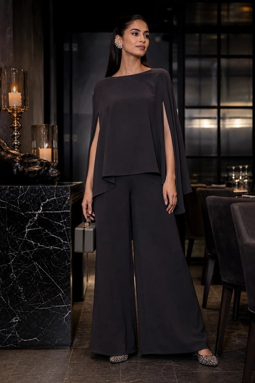 Charcoal Cape Top and Wide-Leg Trousers A woman wears a charcoal cape-style top with wide-leg trousers, embellished pointed shoes, drop earrings, and a small structured handbag.
