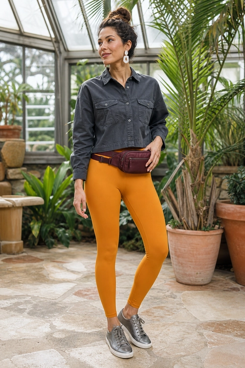 A casual outfit featuring a charcoal button-up shirt, mustard leggings, a burgundy waist bag, and metallic gray sneakers.