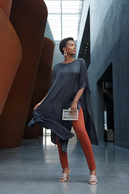 Draped Charcoal Tunic with Rust Leggings A woman wears a flowing charcoal tunic over rust-colored leggings with silver embellished sandals, geometric earrings, and a metallic clutch.