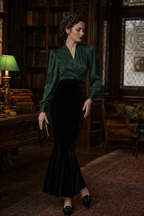 Emerald Blouse and Black Mermaid Skirt A woman wears a dark emerald green long-sleeve blouse with a black floor-length mermaid skirt, pointed-toe shoes, and a black clutch.