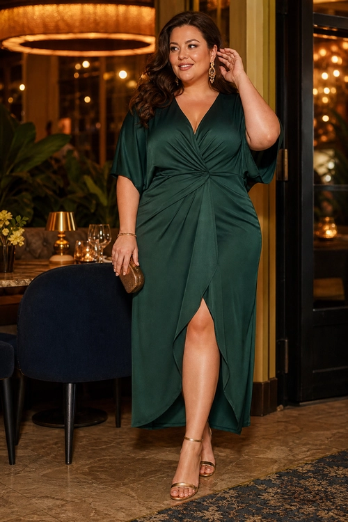 A woman wears an emerald green V-neck wrap-style dress with a front slit, gold earrings, a metallic clutch, and strappy heeled sandals.