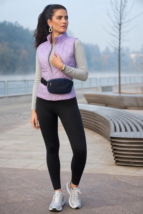 Woman wearing a lavender quilted vest over a gray long-sleeve top with black leggings, gray sneakers, and a black waist bag.