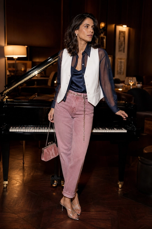 A woman wears a sheer navy blouse with a cream vest, pink trousers, and strappy heeled sandals.