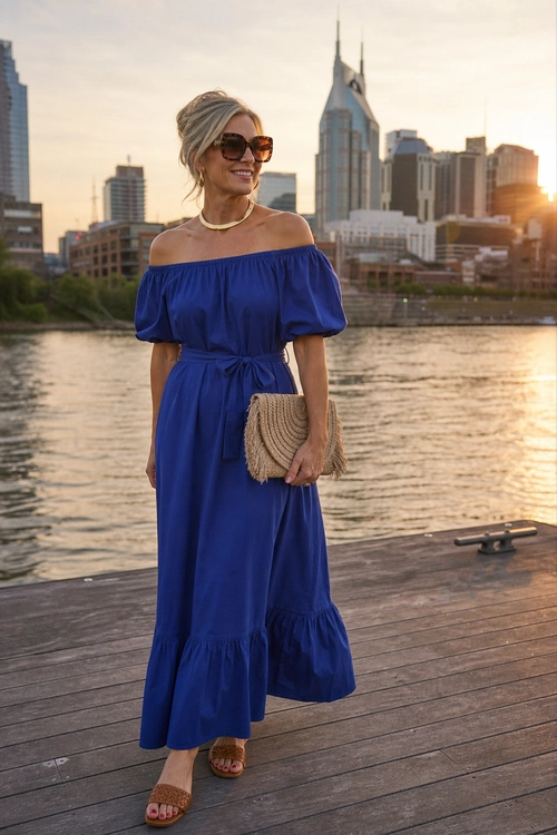 Royal Blue Off-Shoulder Maxi Dress Woman wearing a royal blue off-the-shoulder maxi dress with woven clutch, sunglasses, gold necklace, and tan sandals by the waterfront.