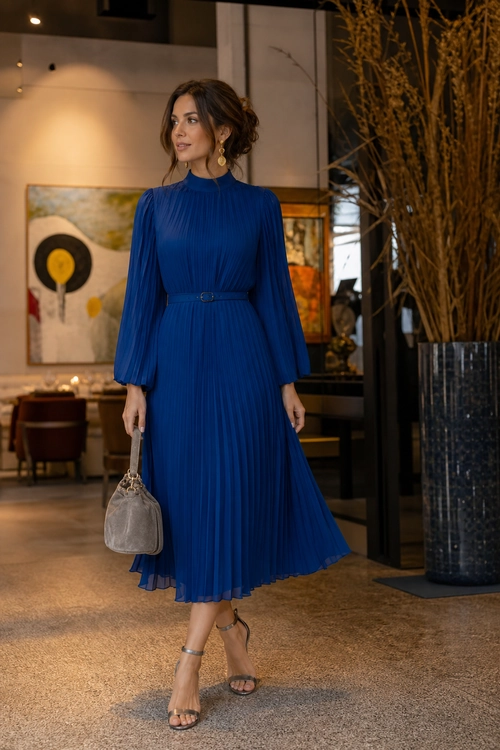 A woman wears a royal blue pleated midi dress with a slim belt, strappy sandals, and a taupe handbag.